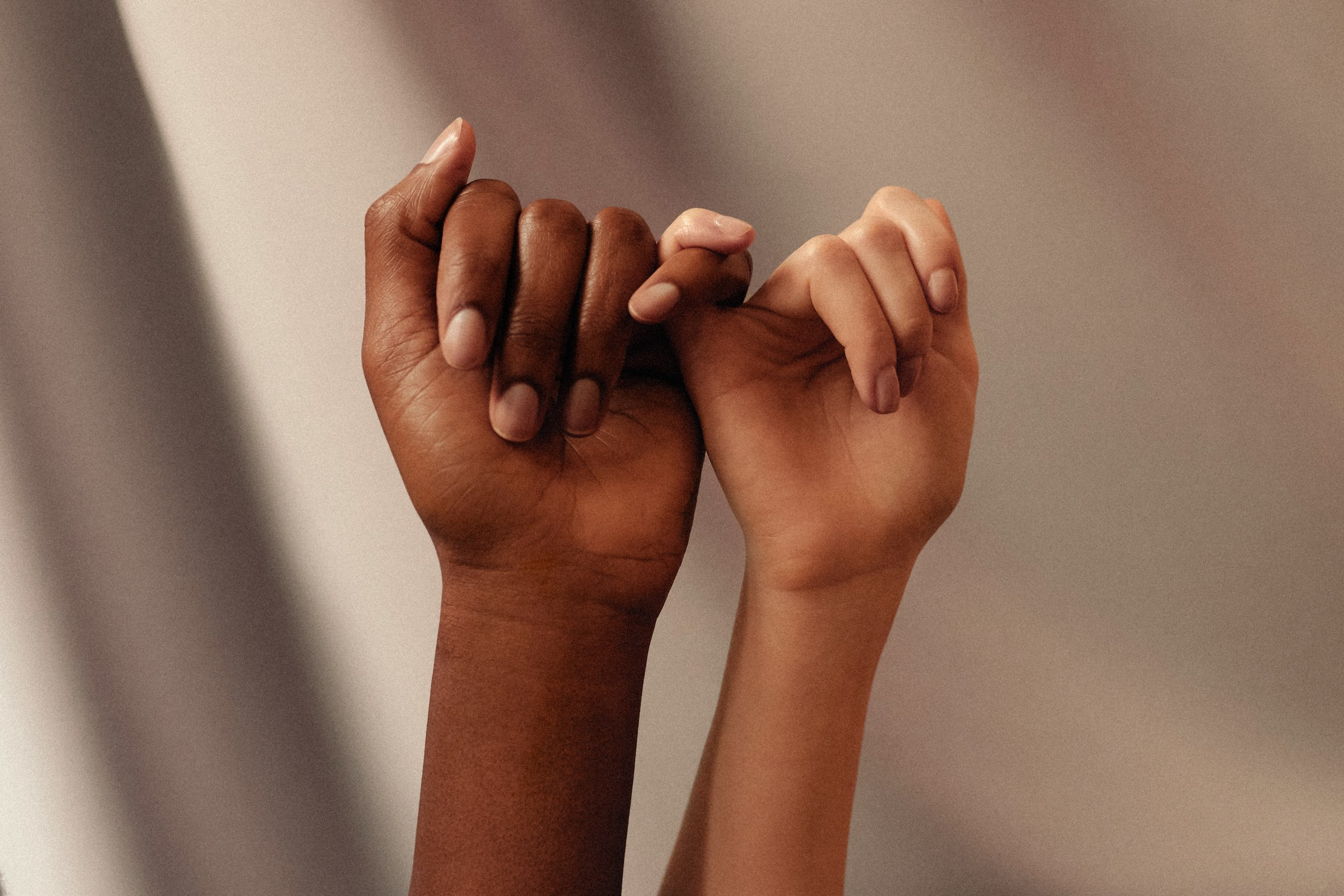 Two hands, one with dark skin and one with light, linked by pinky fingers