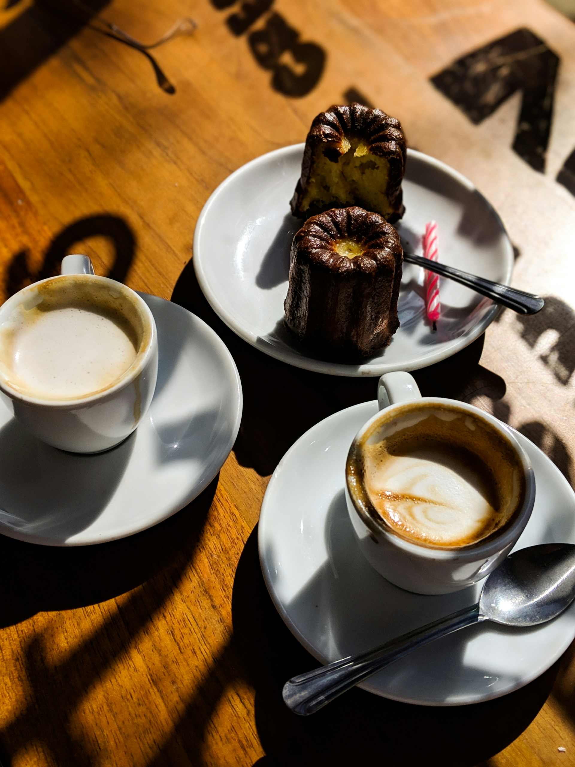 Two coffees on a table with a plate with two cakes and a birthday candle lying next to them on their plage